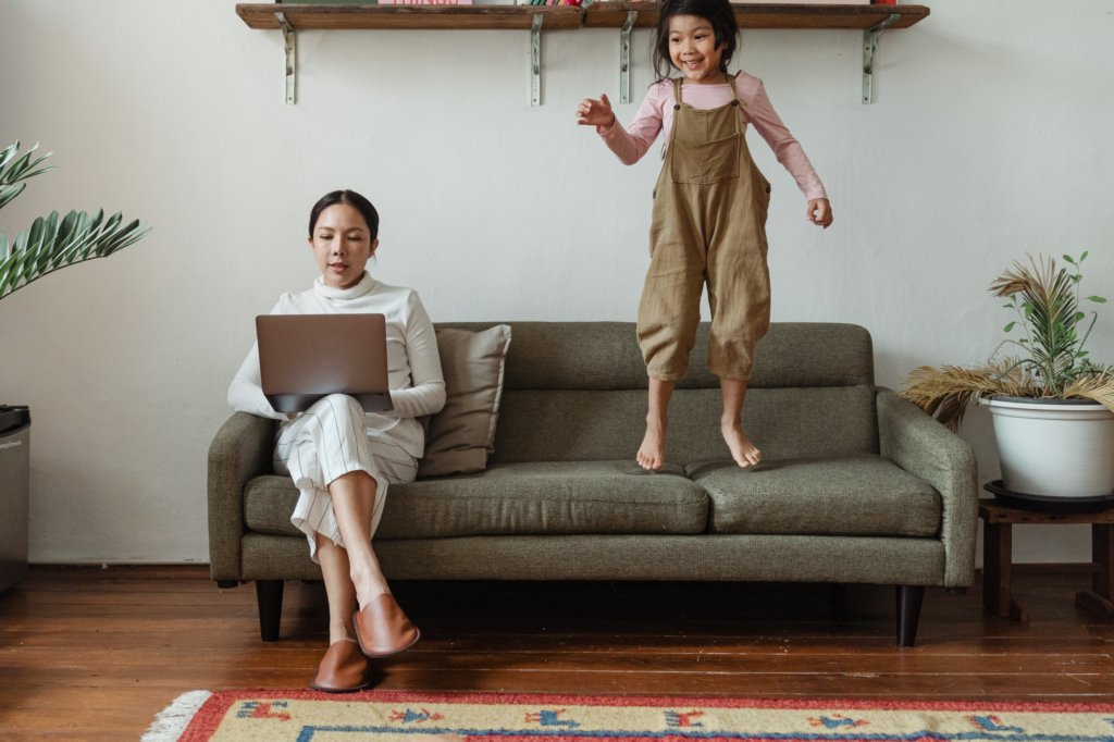 Mother shopping online on couch while daughter plays