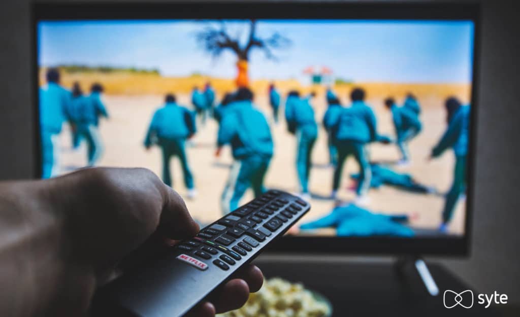 Viewer watches Squid Game on Netflix with remote control in hand. 