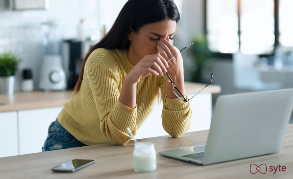 Frustrated woman sits in front of her computer with hand over face after a poor site search experience.