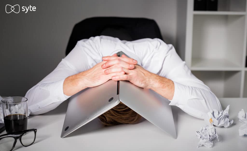 Frustrated man hides under his laptop in frustration after a poor site search experience.