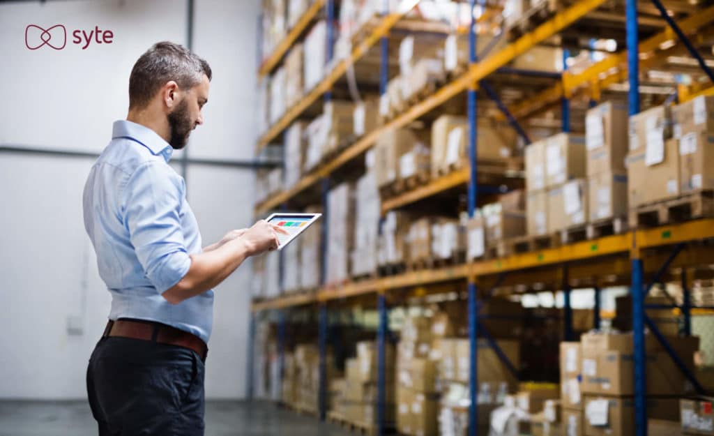 Man checking warehouse inventory and making notes on an iPad. 