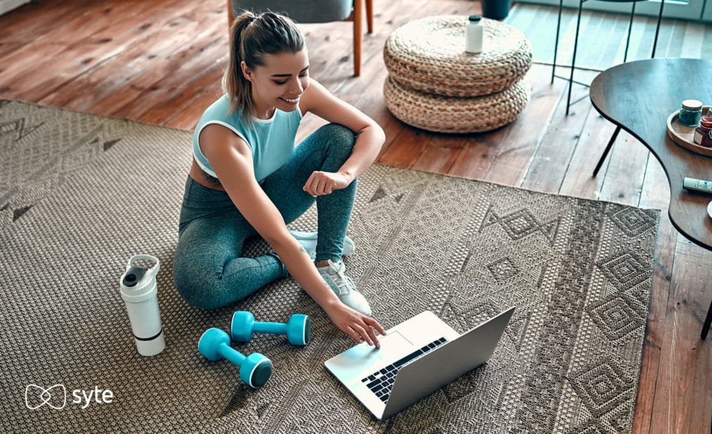 Woman in exercise gear shopping online with a water bottle and weights next to her.