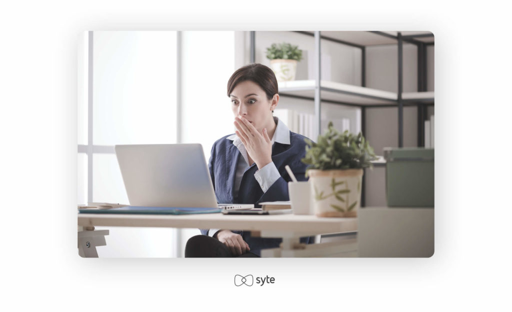 Woman staring shockingly at a screen with a hand over her mouth.