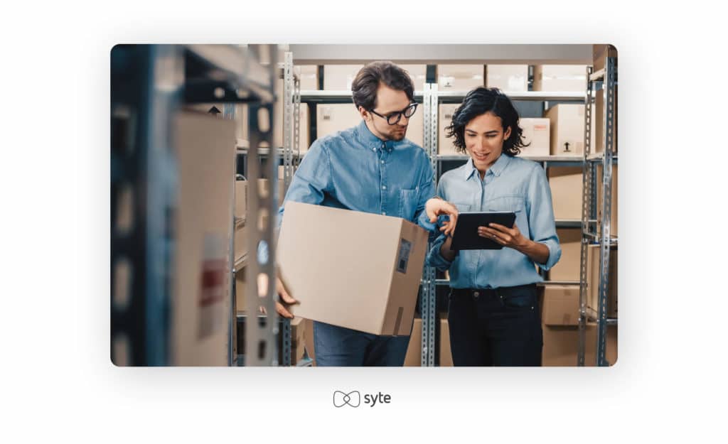 Man and woman talking with a stock of parcels in the background. 